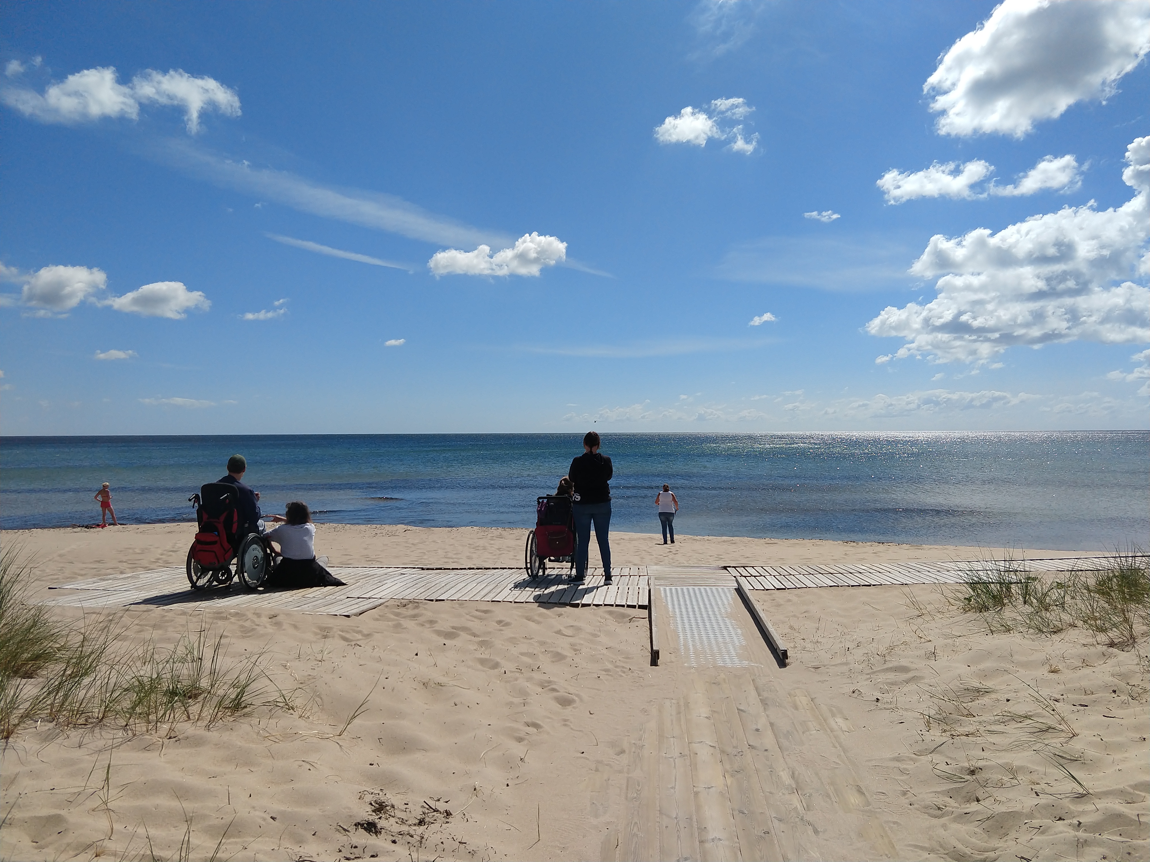 Några personer på en strand tittar ut mot havet och blå himmel med lätta moln