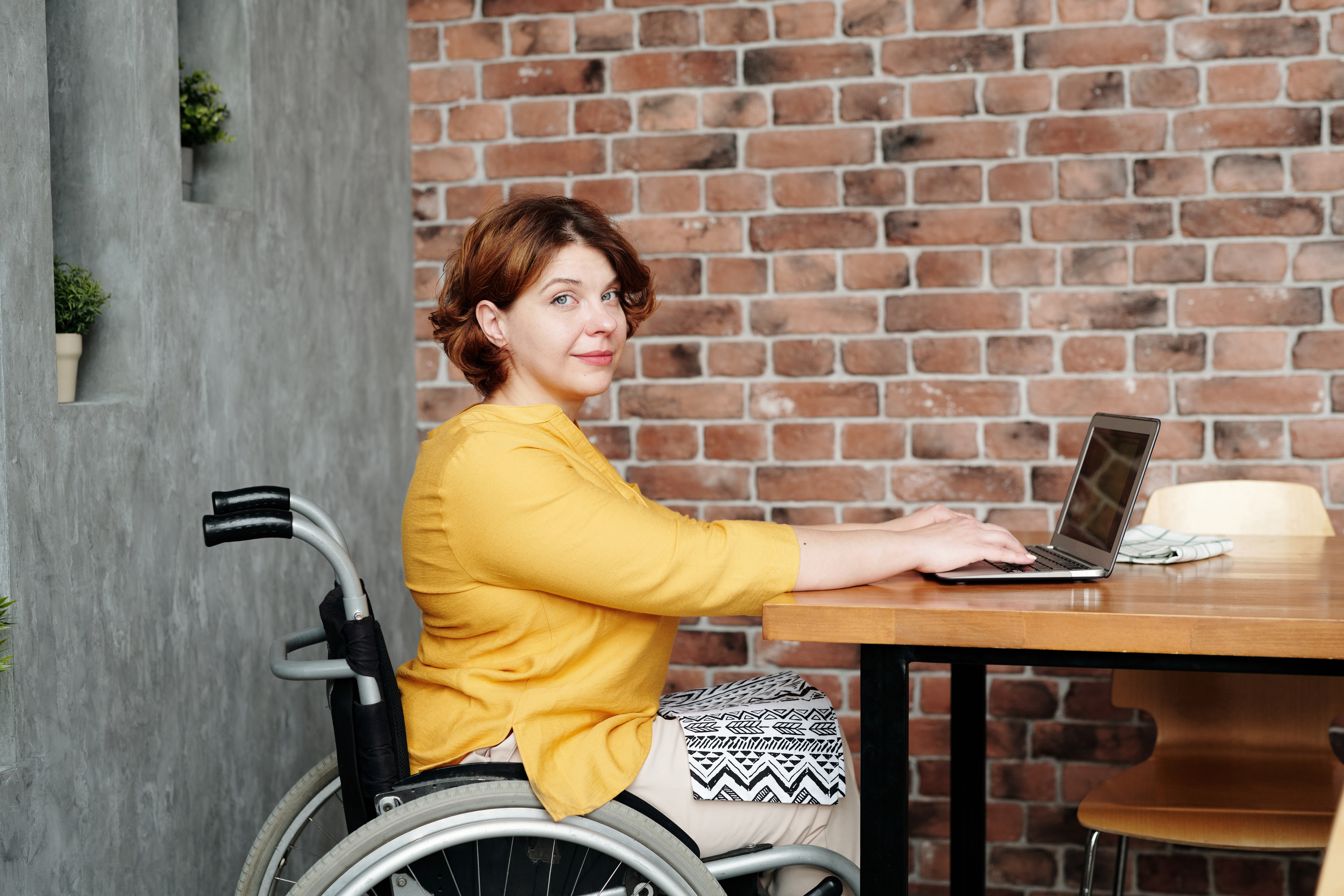 En kvinna i rullstol arbetar med en dator vid ett bord