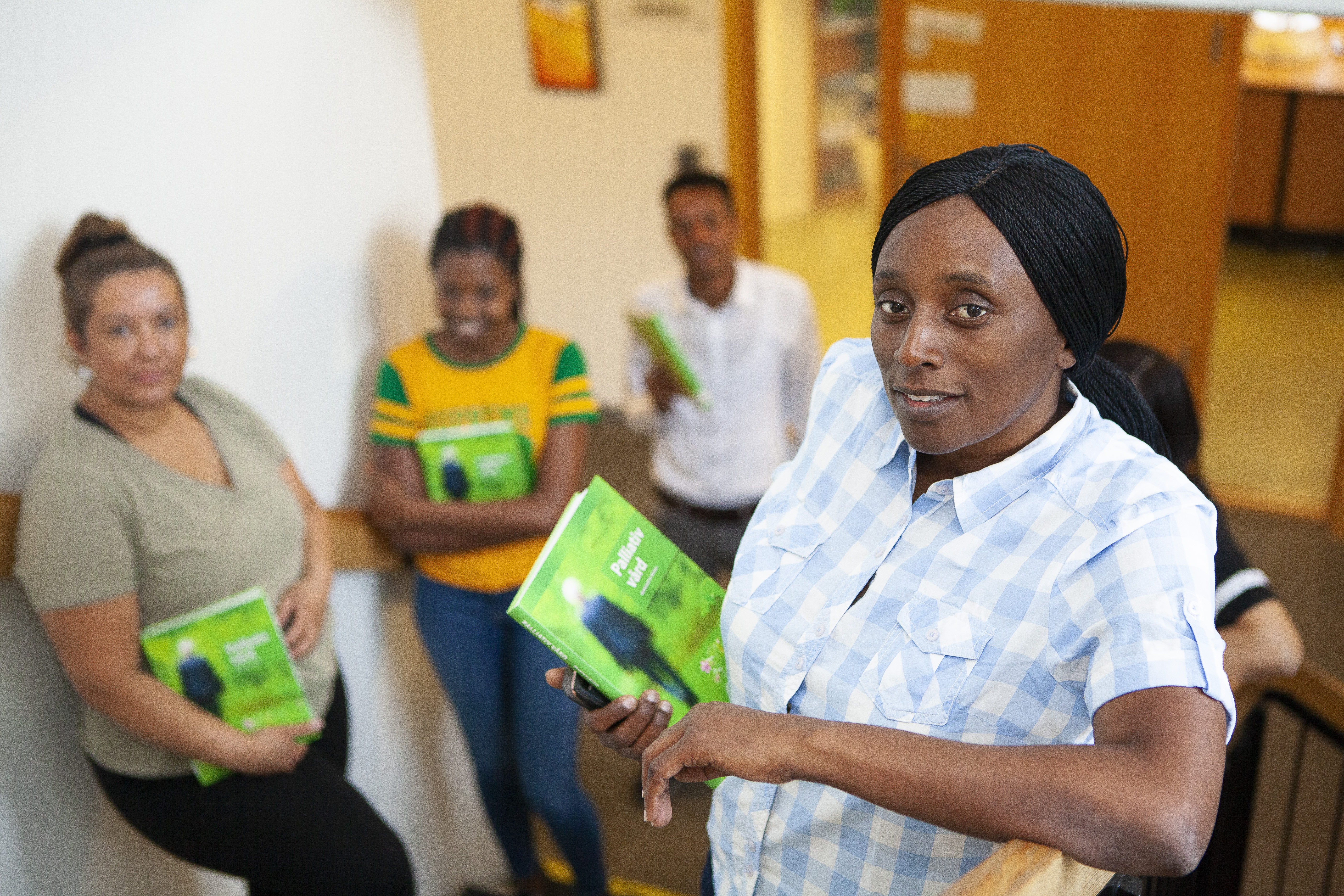 En person med en grön bok om palliativ vård och tre andra personer i bakgrunden