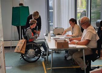 En kvinna röstar i en röstlokal, hon sitter i rullstol.
